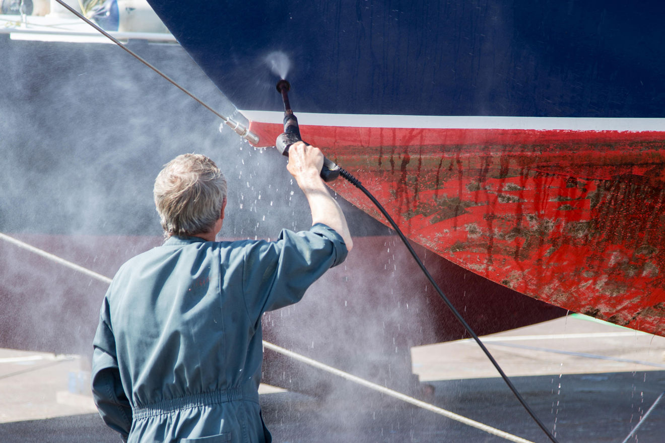man spraying down bottom of boat to remove barnacles and unwanted stuff