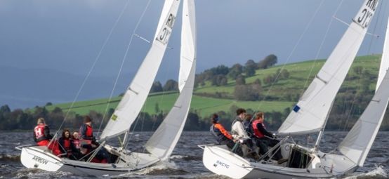 Two teams match racing Sonar keelboats at the Ceilidh Cup in Scotland with grey sky and green hills.