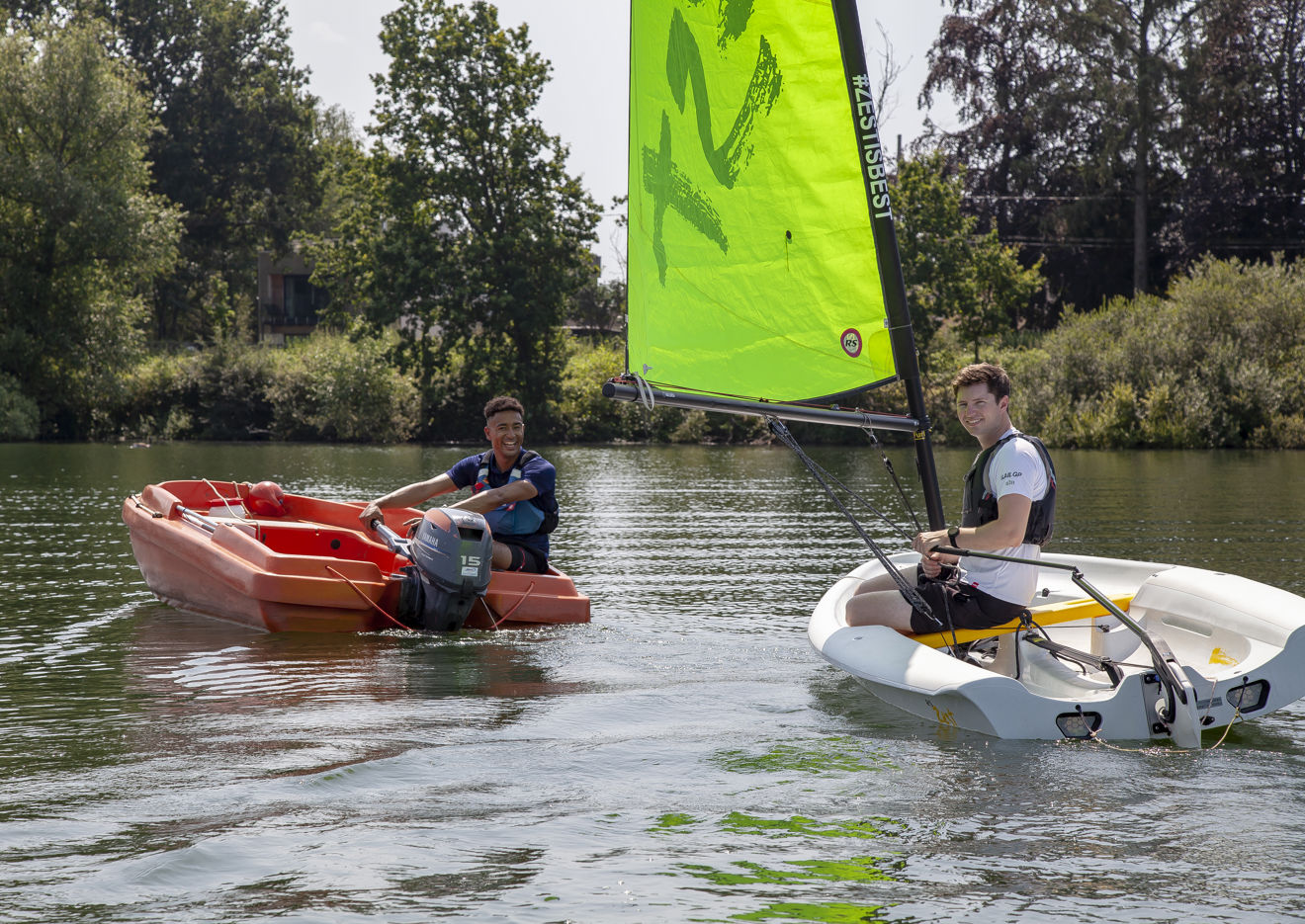 two people sailing in dinghies on a lake, on red dinghy and one white