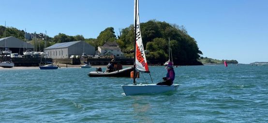 Young sailor on the sea in the sunshine for a Dragon Series event at Port Dinorwic SC in Wales with coach boat nearby, blue waters and sky and beautiful shoreline in the background.