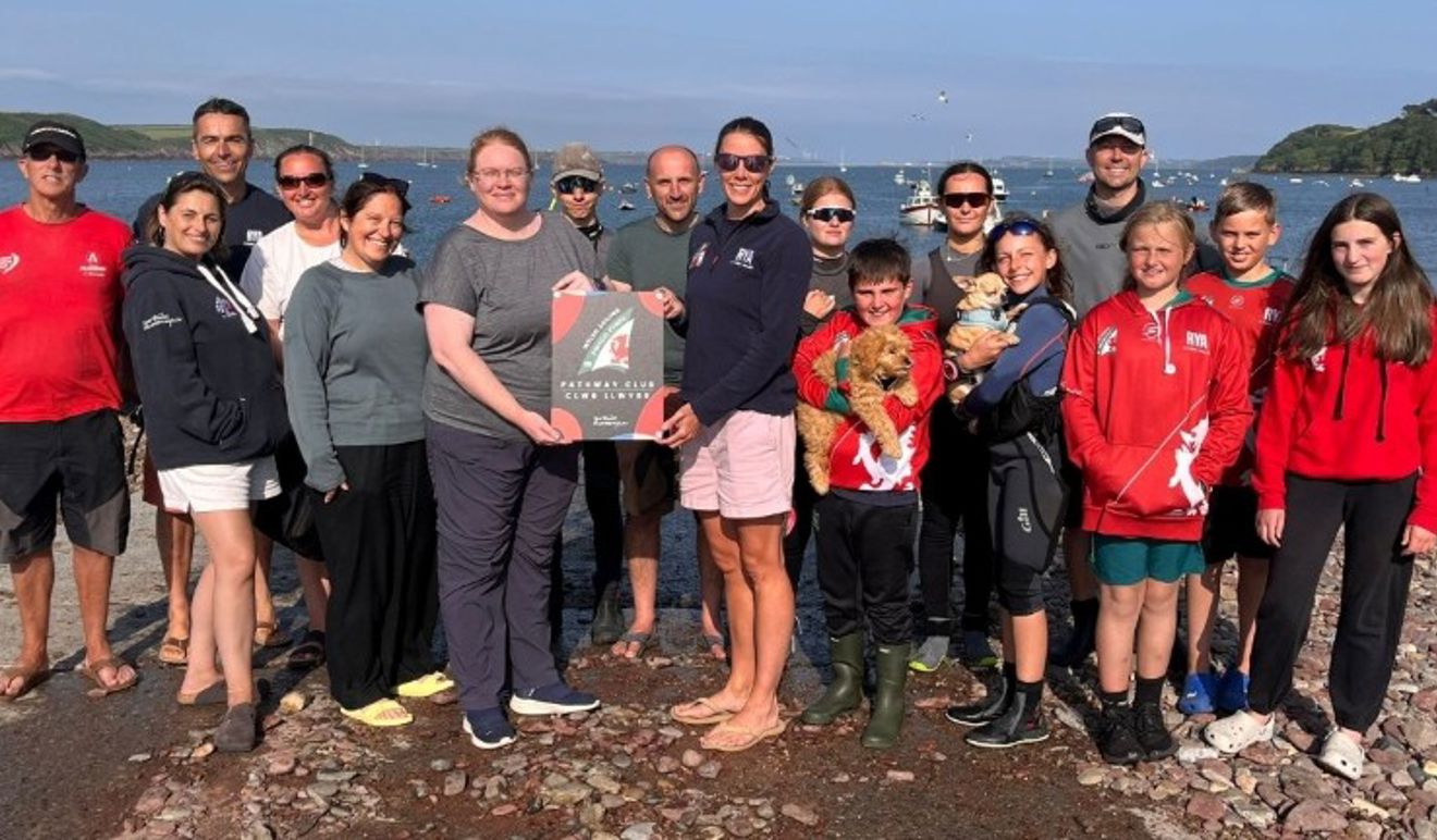 Group picture with RYA CW Performance Manager Sarah McGovern presenting a Pathway Club plaque to members of Neyland Yacht Club's youth and junior section.
