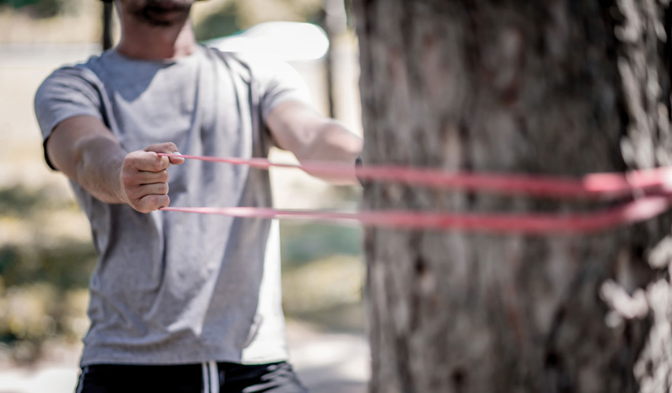 	An image of a man performing exercise using the Pilates band wrapped around a tree