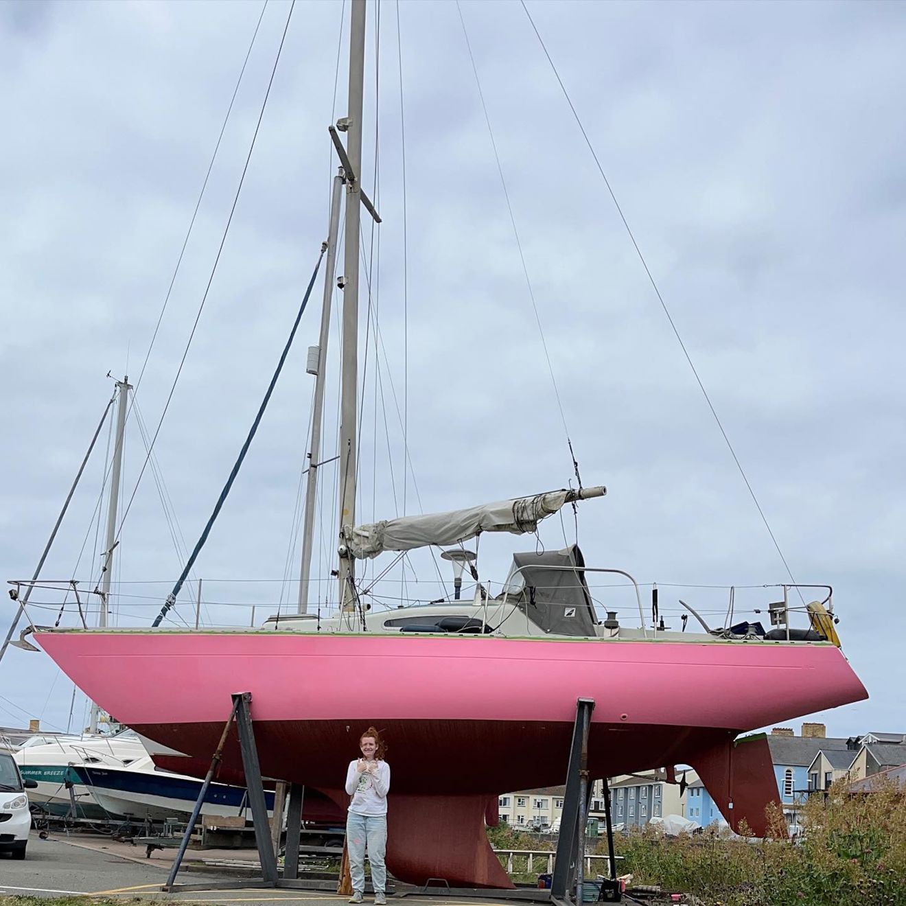 	Freya Terry stood in front of the hull of her pink painted yacht Pink Delta which is in a boat yard on shore.