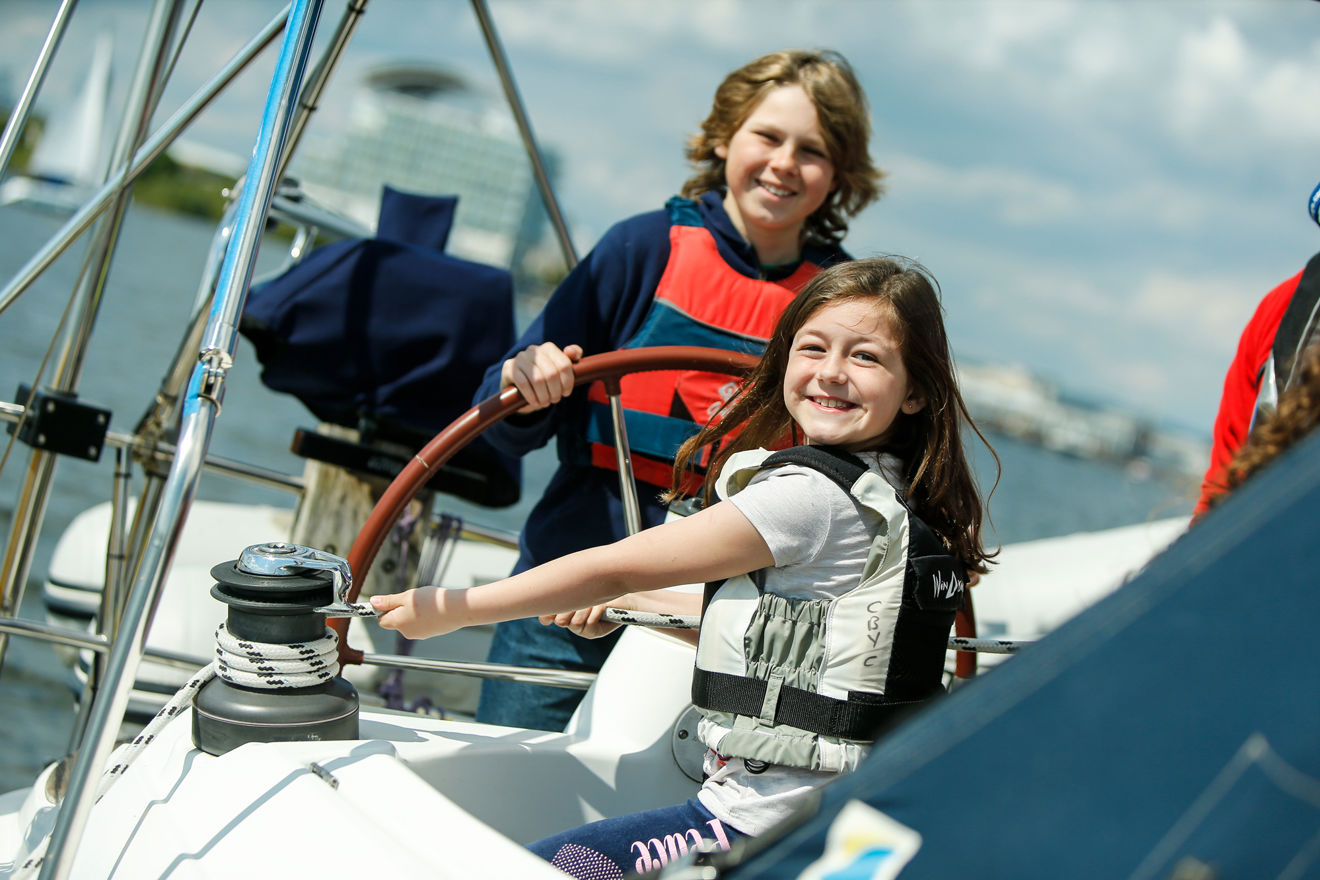 a youny boy and girl on a yacht, the young boy is steering and young girl is pulling the rope