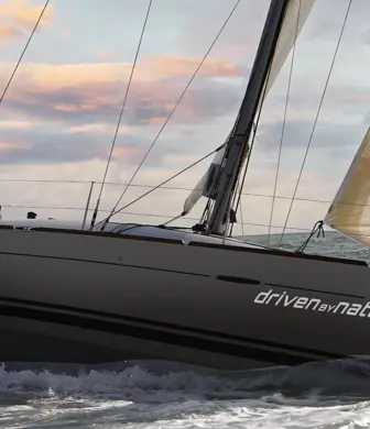 A yacht from Driven by Nature sailing with one sail up with grey and orange clouds in the sky at dusk