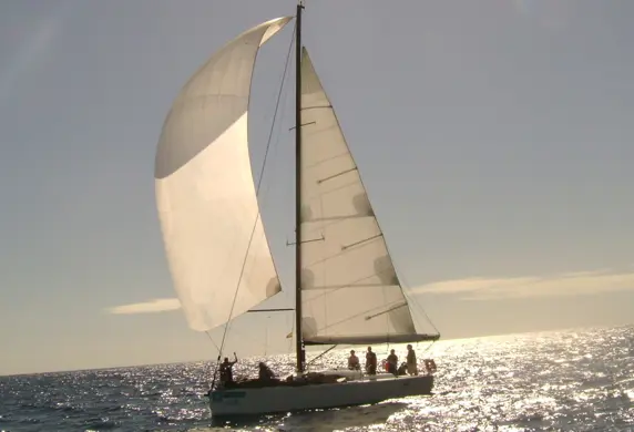 People on board a yacht with a mainsail and spinnaker up on a clear day with the sun glinting off the water