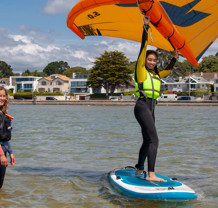 Woman learning to wingsurf, she is on the board, and instructor is in the water