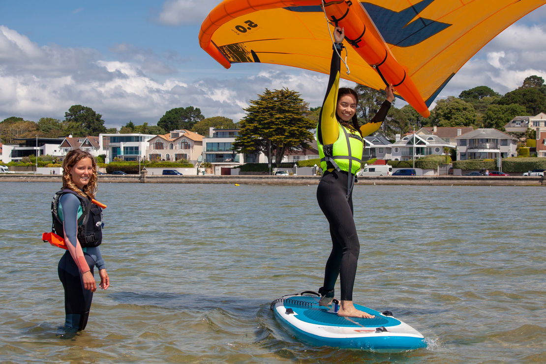 Woman learning to wingsurf, she is on the board, and instructor is in the water