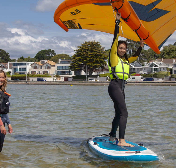 Woman learning to wingsurf, she is on the board, and instructor is in the water