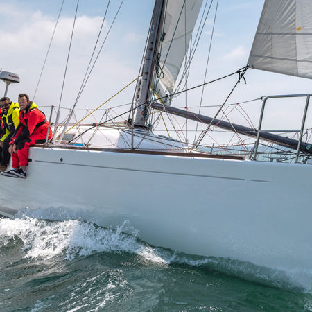 numerous people sat over the side of a sailing yacht whilst sailing on the ocean