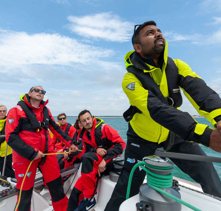 Numerous people on board a yacht, one steering and the others doing rope work.
