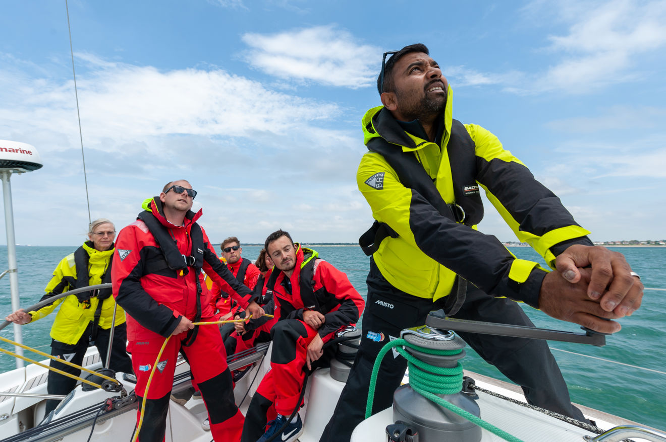 Numerous people on board a yacht, one steering and the others doing rope work.