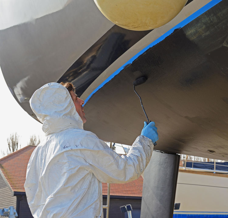 Man antifouling his boat with protective gear and paint