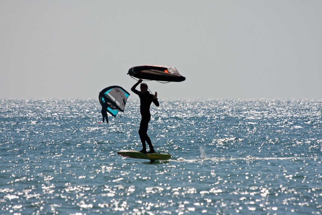 a silhouette of two wing surfers travelling through sparkling water