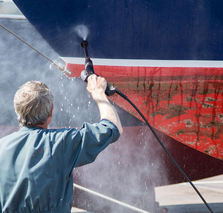 man spraying down bottom of boat to remove barnacles and unwanted stuff
