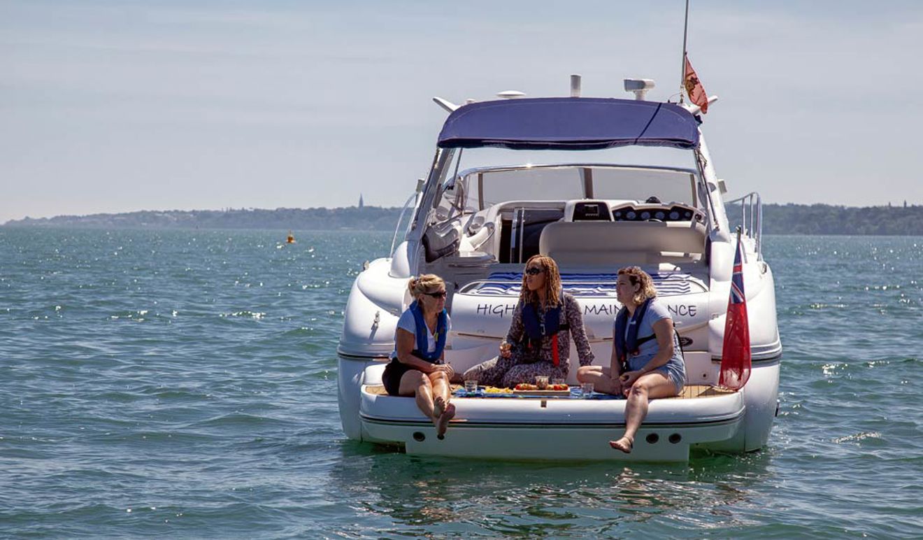 three women sitting on the back of a motor cruiser talking and enjoying food