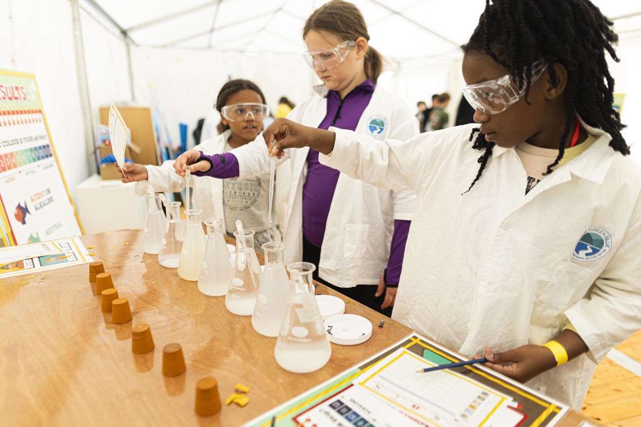 An image of 3 female students performing chemical reactions where all of them are wearing protective glasses
