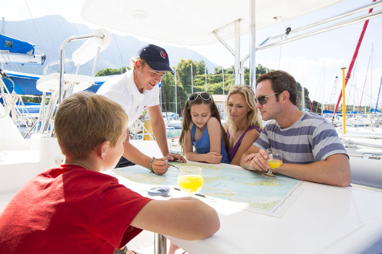 An image of family sitting by a boat with a man showing them a route on the map