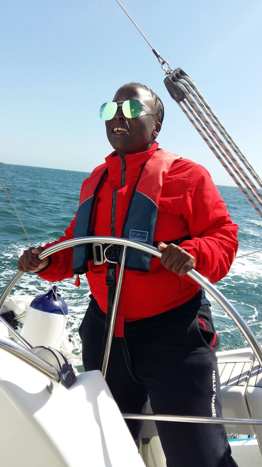 woman steering yacht on the open ocean, she is wearing reflective sunglasses and a life jacket
