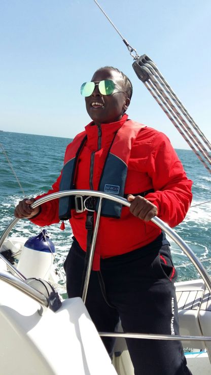 woman steering yacht on the open ocean, she is wearing reflective sunglasses and a life jacket