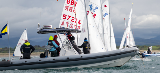 Long shot of crew on powerboat looking out at sailboats