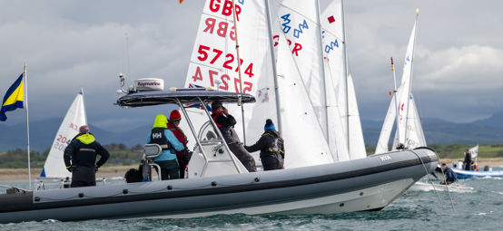Long shot of crew on powerboat looking out at sailboats