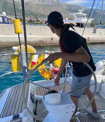 A young man on a sailing yacht looking backwards whilst steering the yacht into the marina at Yacht Sail Training School, Brac Island, Croatia