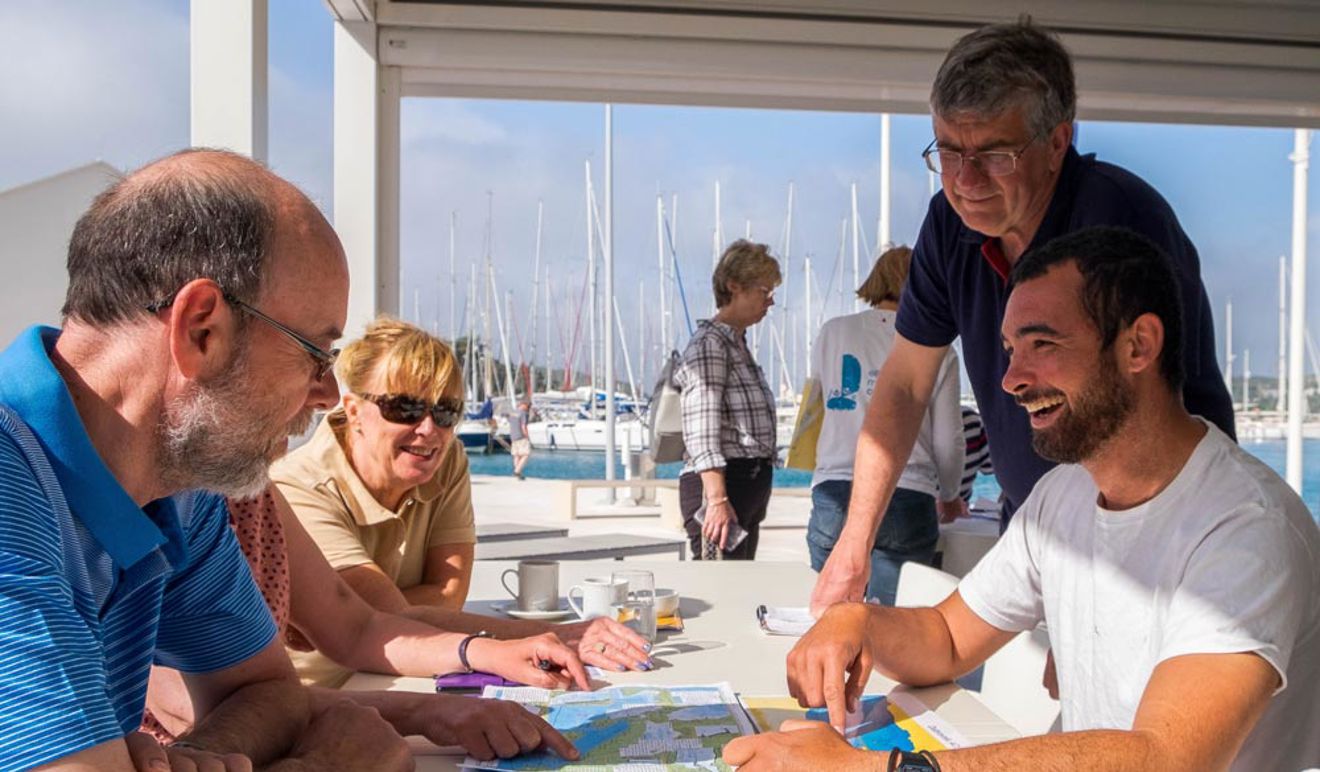 group of people sat at a table on the shore looking at a map