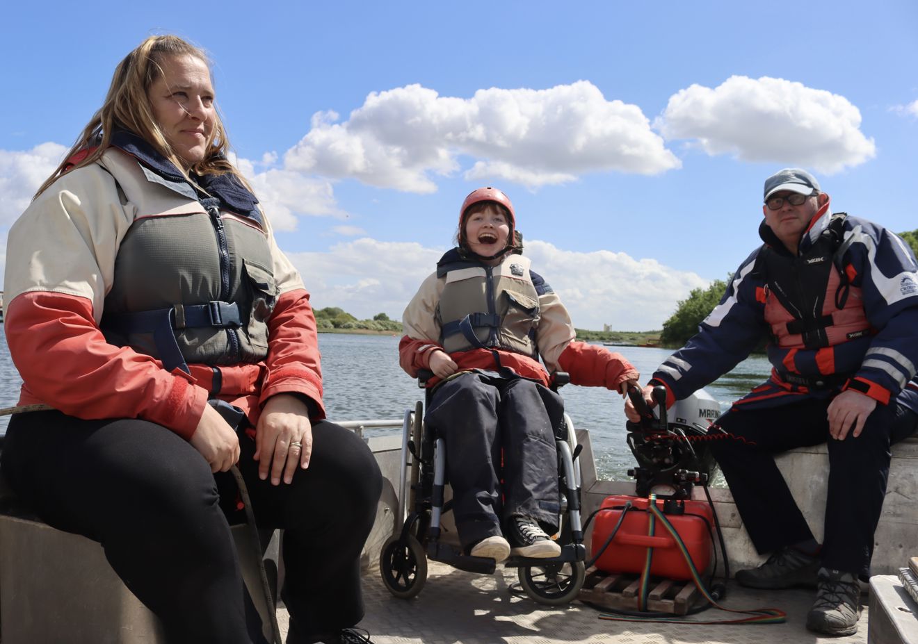 Grace and her carers laughing and smiling on a boat