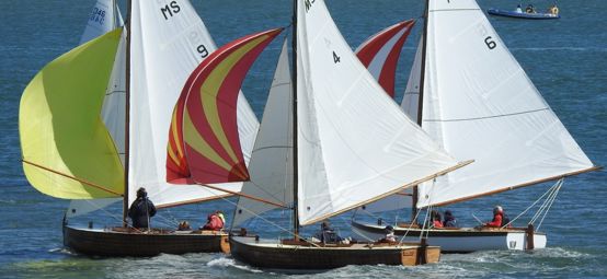 Three dayboats with colourful spinnakers on a sunny day competing in the Menai Strait Regattas in North Wales.