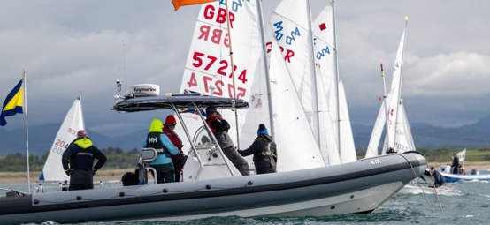 Youth boats lining up for a start next to committee boat with mountains in the background. 