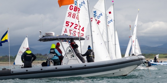 Youth boats lining up for a start next to committee boat with mountains in the background. 