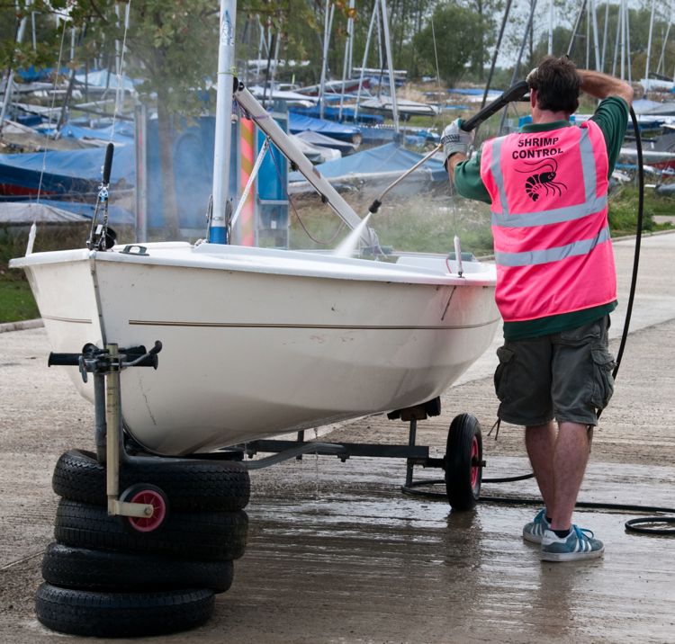 man hosing his dinghy whilst on shore on wheels
