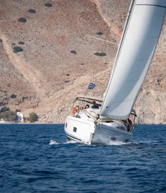 A head-on shot of a sailing yacht with the mountains of Aegina, Greece in the background