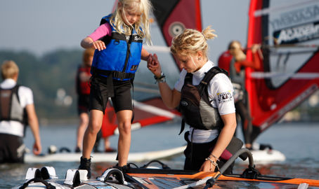 Instructor helping young girl onto windsurfing board