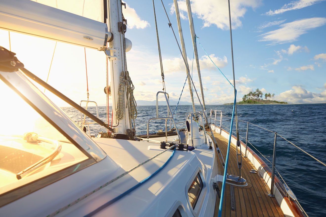 close of of the side and front of a sailing yacht taken from the side/back of the yacht, with the sun glaring through the glass