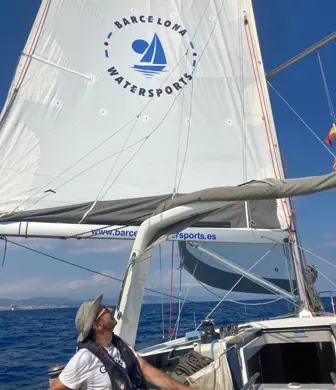 A man on a yacht looking up at the mainsail with the words Barcelona Watersports on it