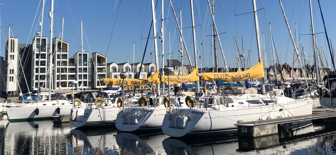 Lots of yachts moored in a marina with blocks of apartments in the background against a beautiful blue sky