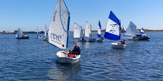 Young Optimist sailor on the water with more boats in the background on a sunny day with blue skies at Cardiff Bay YC.