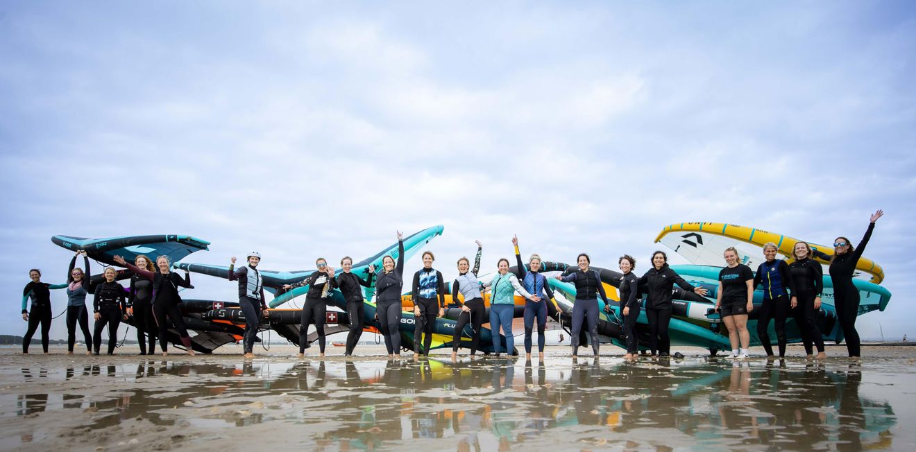 Group photo of numerous women standing on the beach cheering