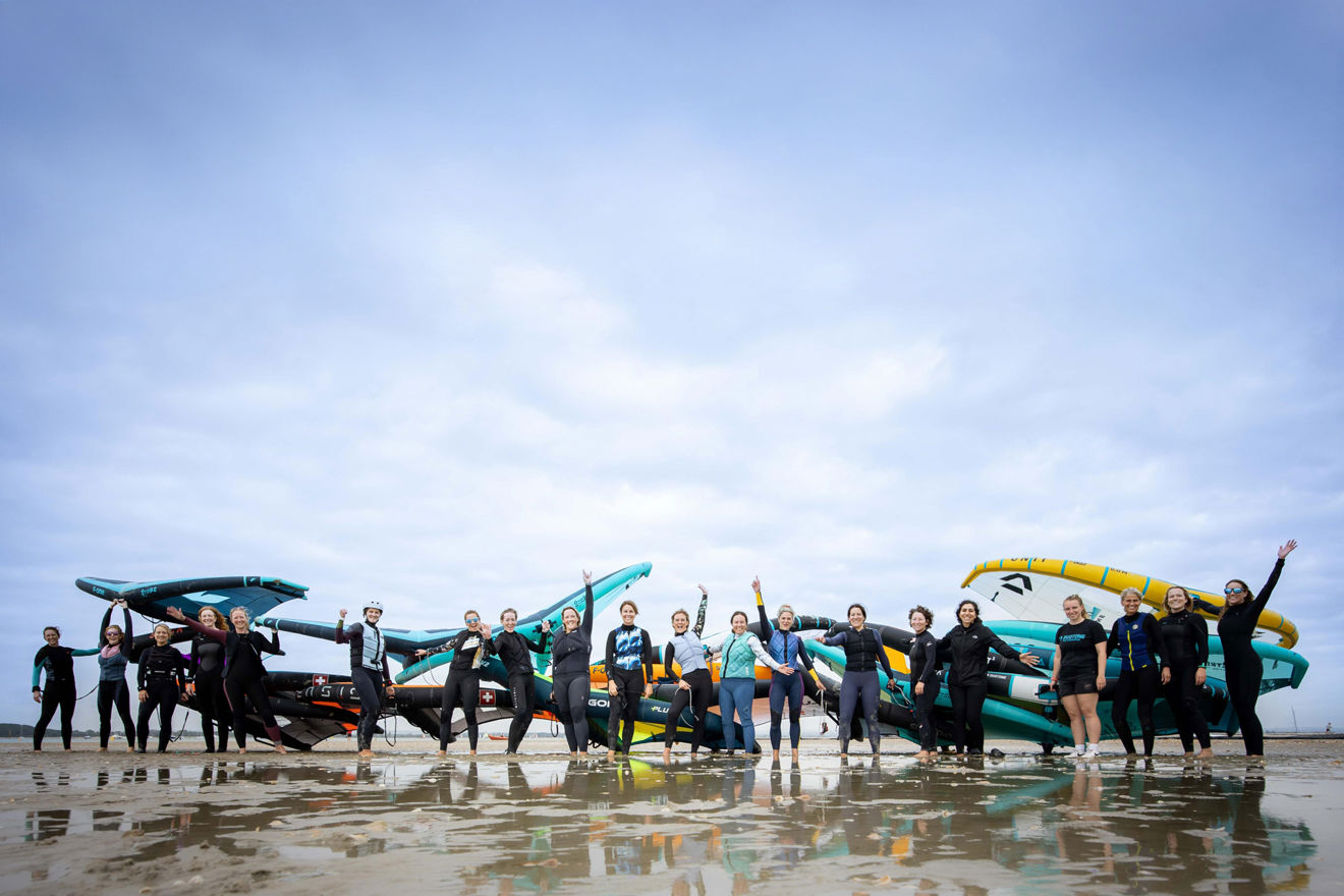 Group photo of numerous women standing on the beach cheering
