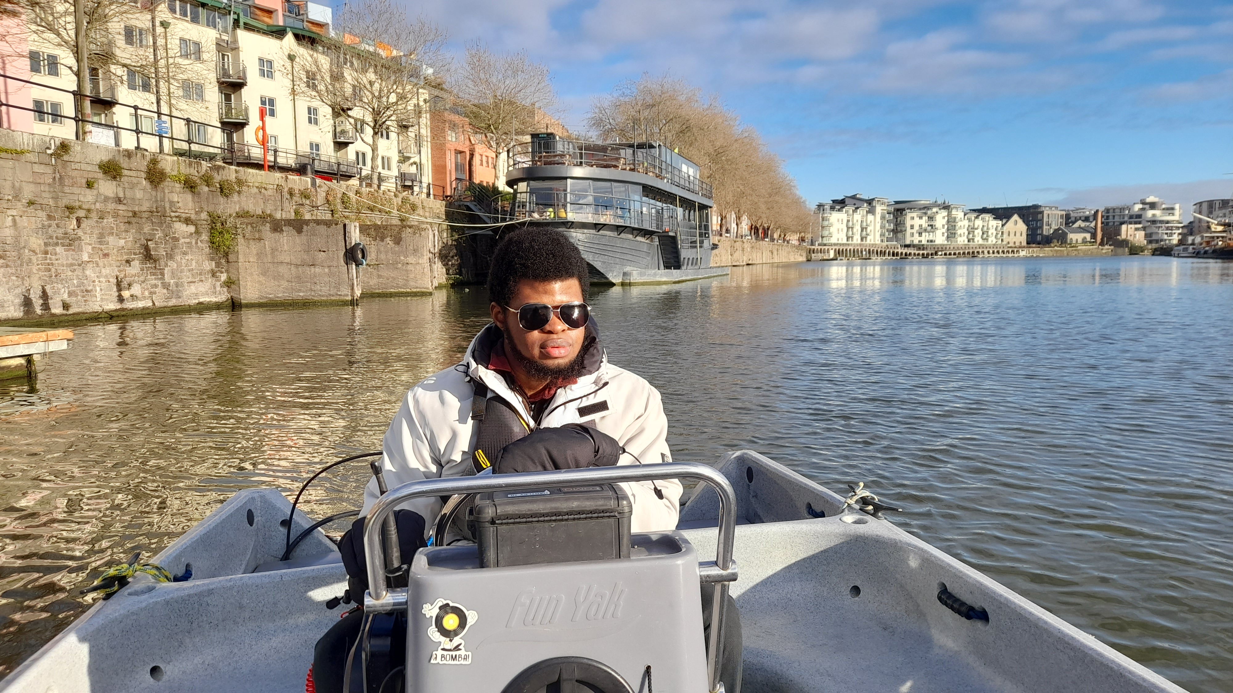 mid-shot of young man driving motorboat on a city river on sunny day
