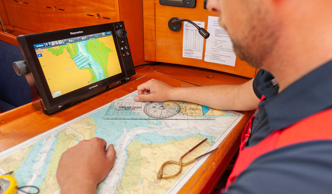 man looking at map laid out in front of him, along with electronic navigation device