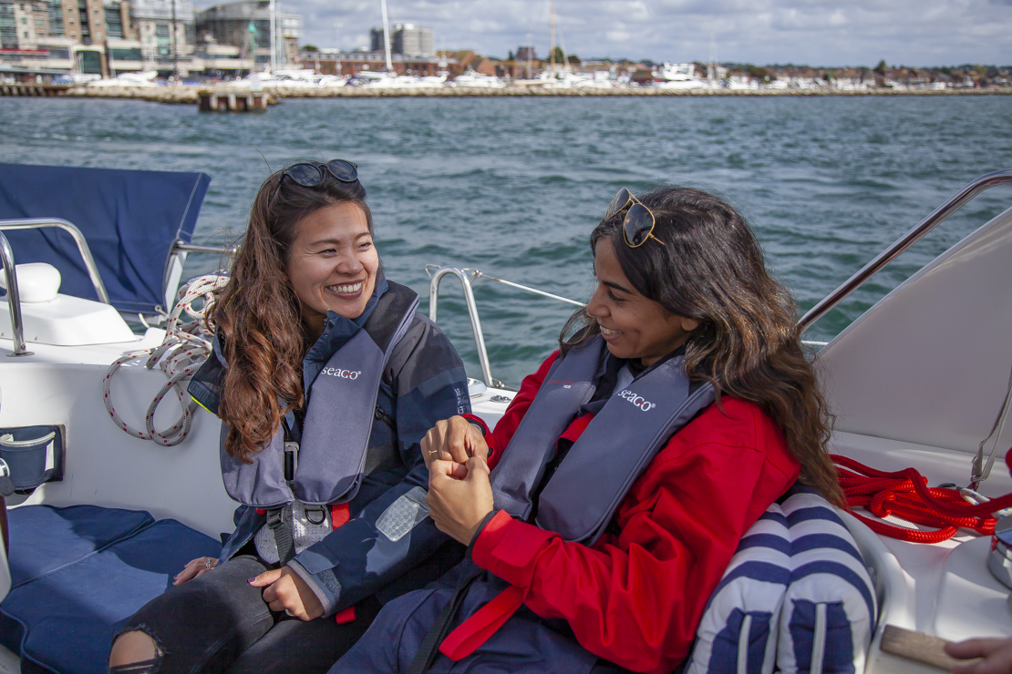 two women sitting on a large yacht smiling at each other
