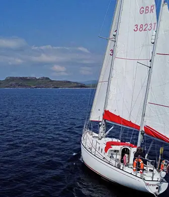 A training yacht sailing on the open sea with three sails up and the land in the distance from Ardent Training, Argyll, Isle of Mull