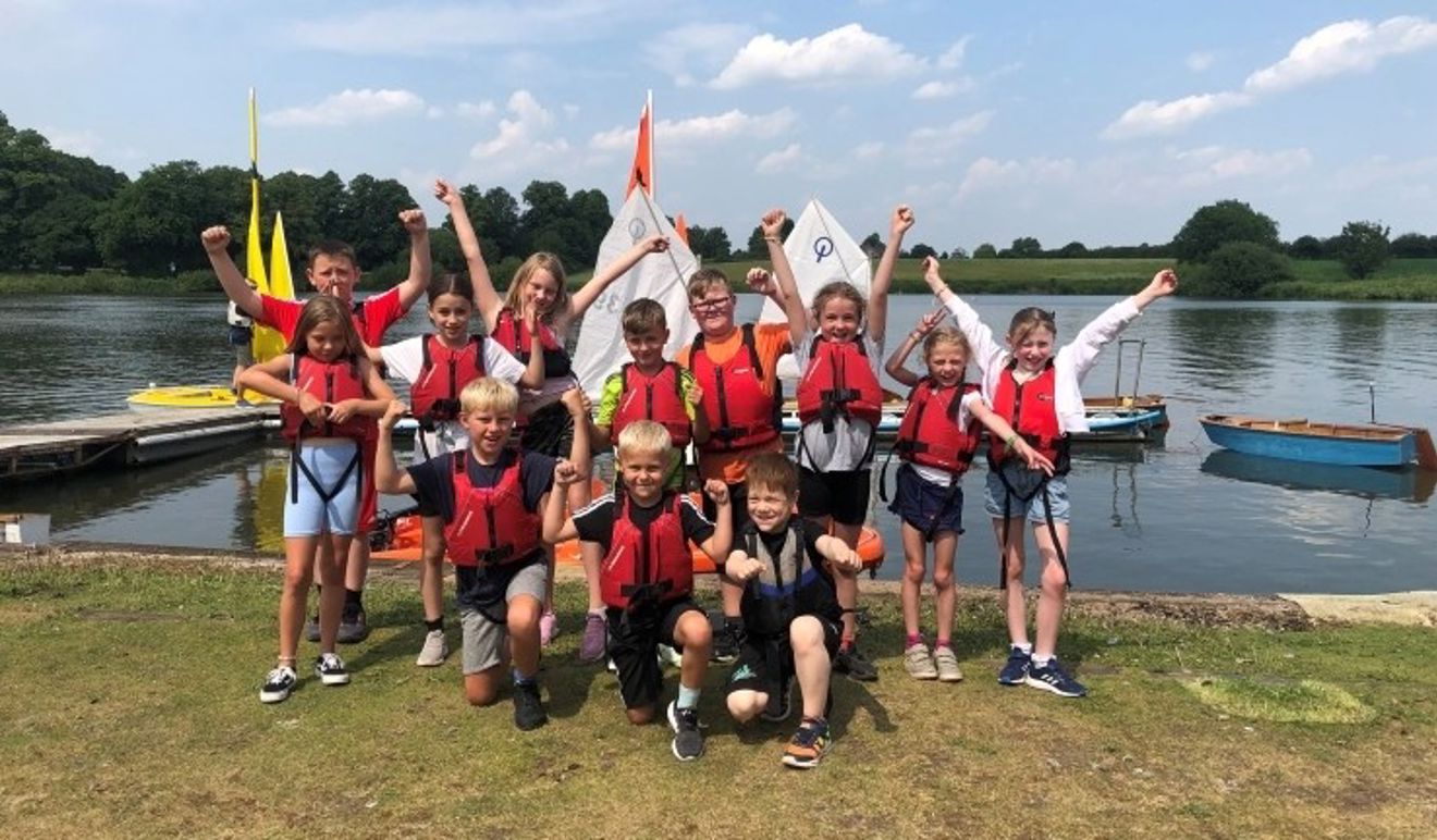 Group of cheering children in red buoyancy aids on shore at Gresford SC during an All Afloat session.