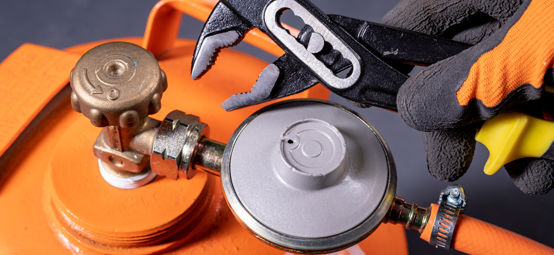 	An image of orange Gas cylinder with a person holding one of the tools to fix the nasal of cylinder