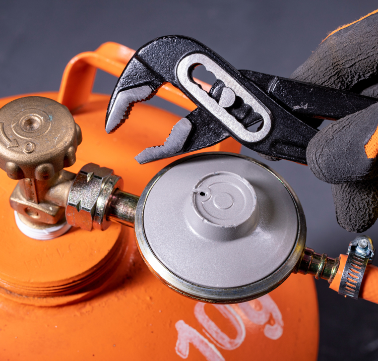 An image of orange Gas cylinder with a person holding one of the tools to fix the nasal of cylinder