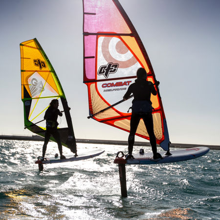 a silhouette of two foiling windsurfers against the sun and sea