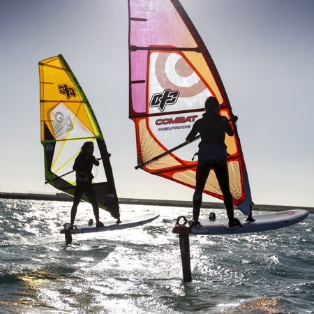 a silhouette of two foiling windsurfers against the sun and sea